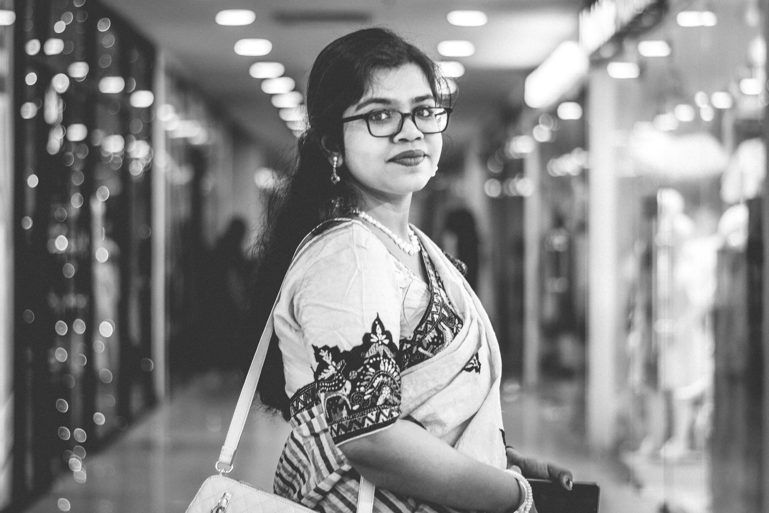 Black and white portrait of a woman in traditional attire shopping in a modern mall.